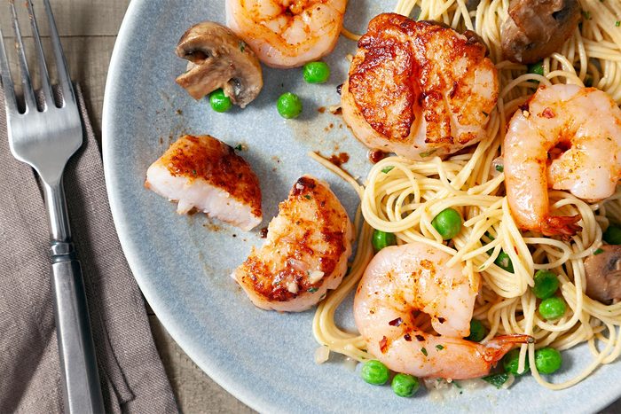 Close shot of Sauteed Scallops & Shrimp Pasta; served in plate; sprinkle with parsley; fork; napkin; wooden background;
