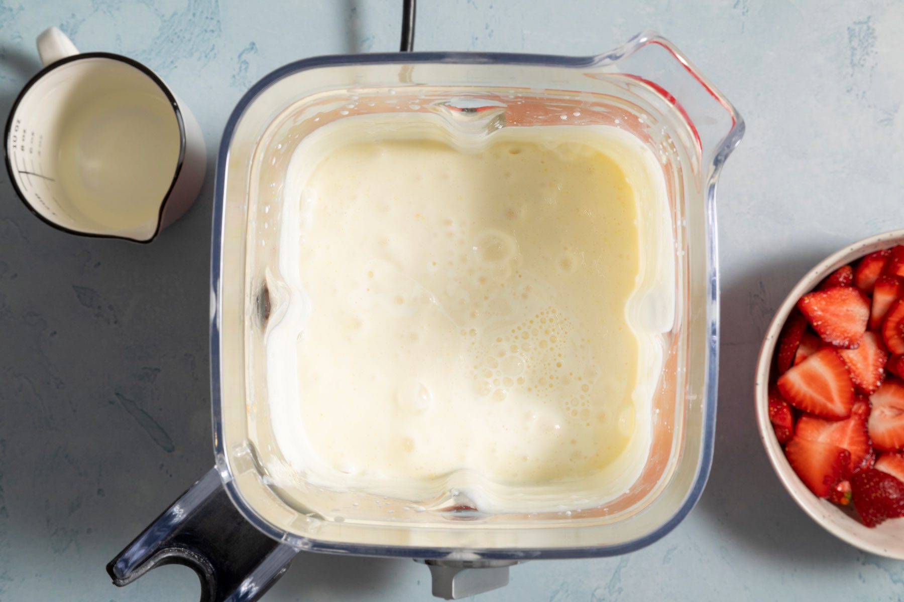 Cream cheese mixture in a blender with a bowl of strawberries on the side