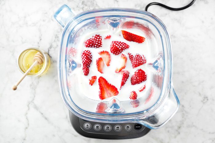 overhead shot of strawberries in a blender with milk on marble surface