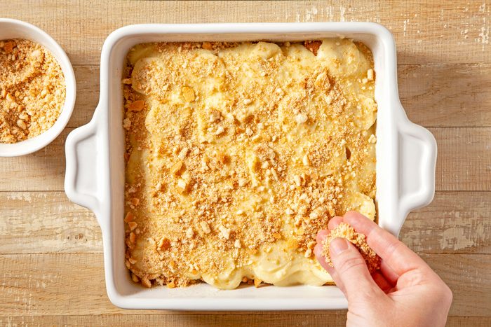 A hand is sprinkling wafers over the surface of the pudding in a baking dish