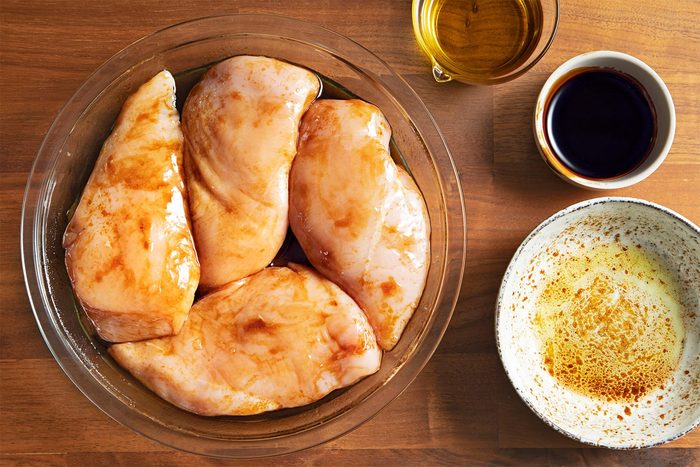Overhead shot of marinated chicken breats; in a shallow dish; oil; balsamic glaze; salt; brown wooden background;