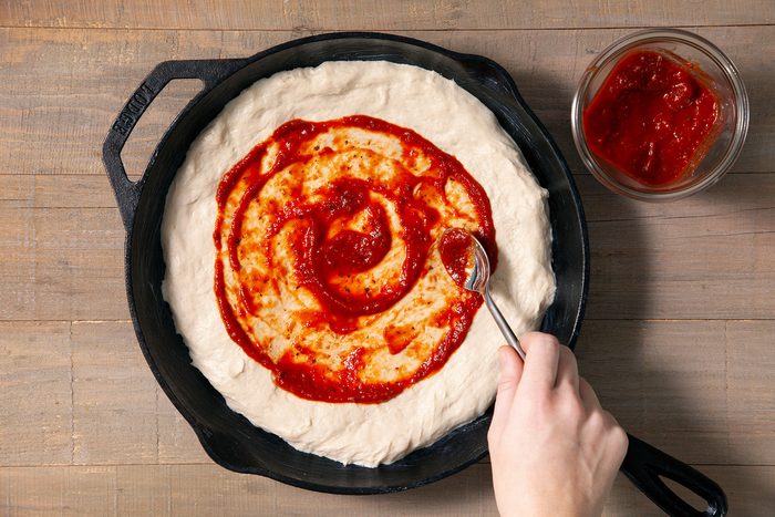 Spreading pizza sauce on dough