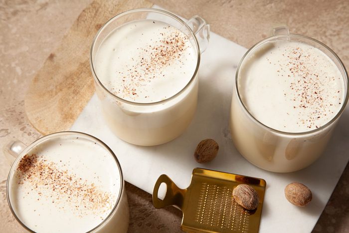 Overhead shot of Homemade Eggnog; in glass jar; serve in three glasses on white tray; sprinkle with additional nutmeg before serving; light brown marble background;