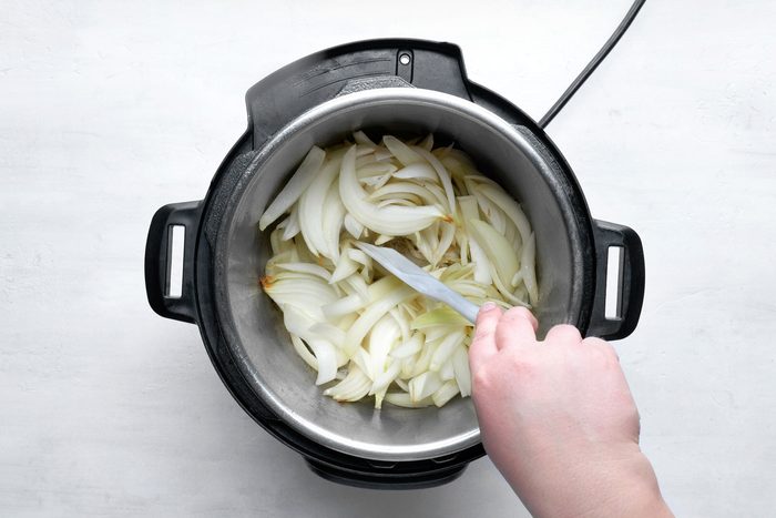 overhead shot; white background; cooking onions in electric pressure cooking using spatula;