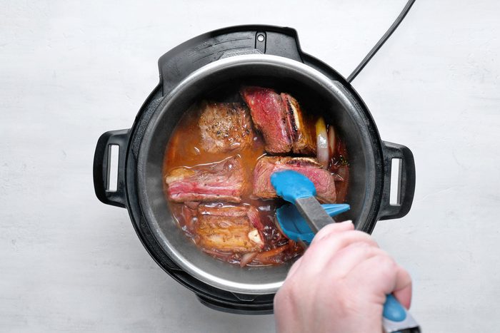 overhead shot; white background; Adding ribs to cooker using tongs;