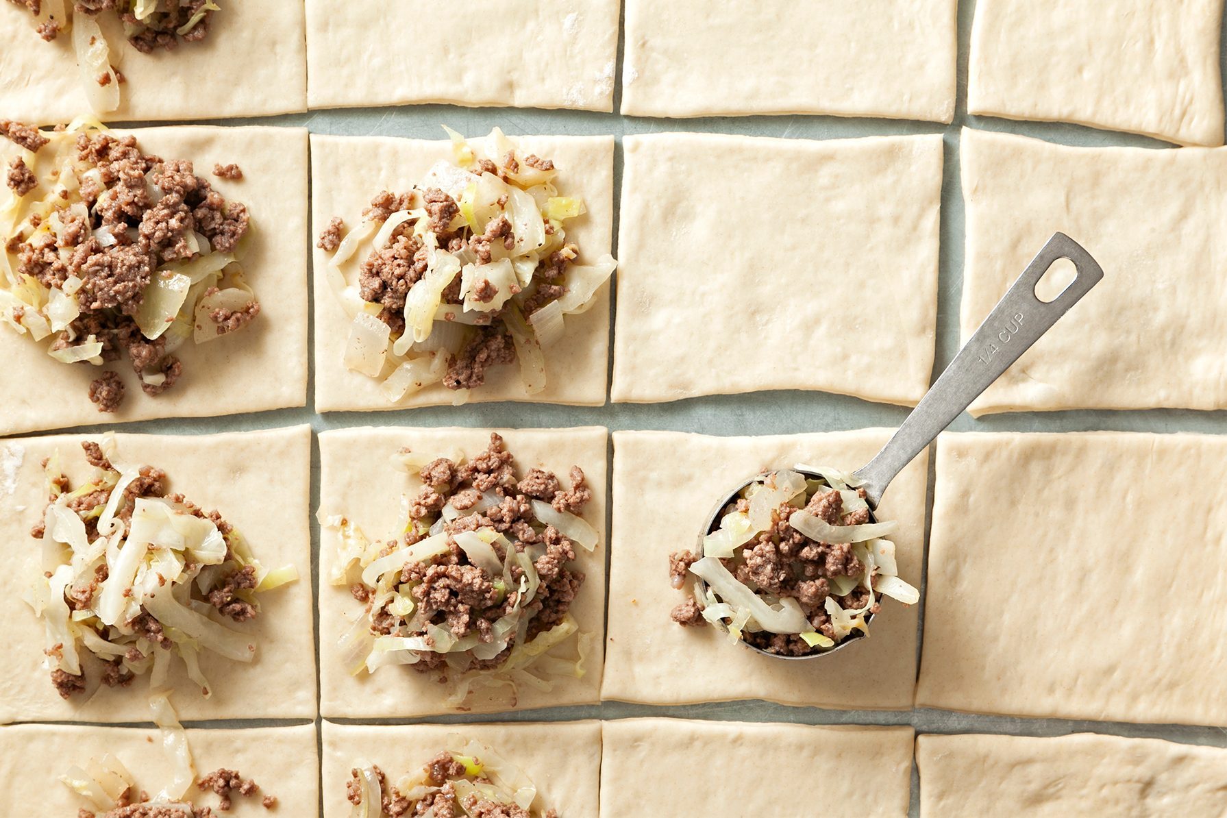 Square pieces of dough arranged in a grid, each topped with a mixture of cooked minced meat and shredded cabbage.