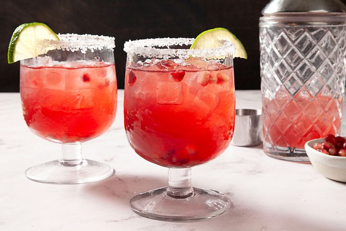 Pomegranate Margarita served in two glass and garnished with lime wedge and pomegranate seeds and shaker on the side
