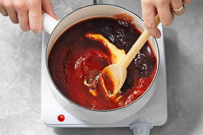 A hand is mixing sauce with other ingredients in a saucepan