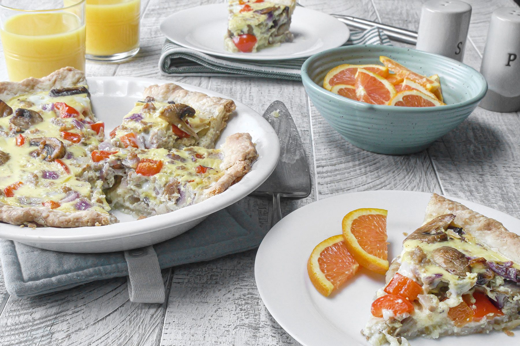 Quiche served on plate with orange juice and slices of oranges
