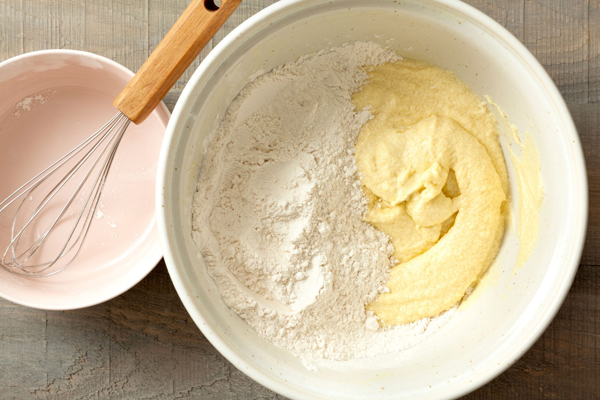 all purpose flour and butter-sugar mixture in a large bowl on wooden surface with a whisk placed next to it.