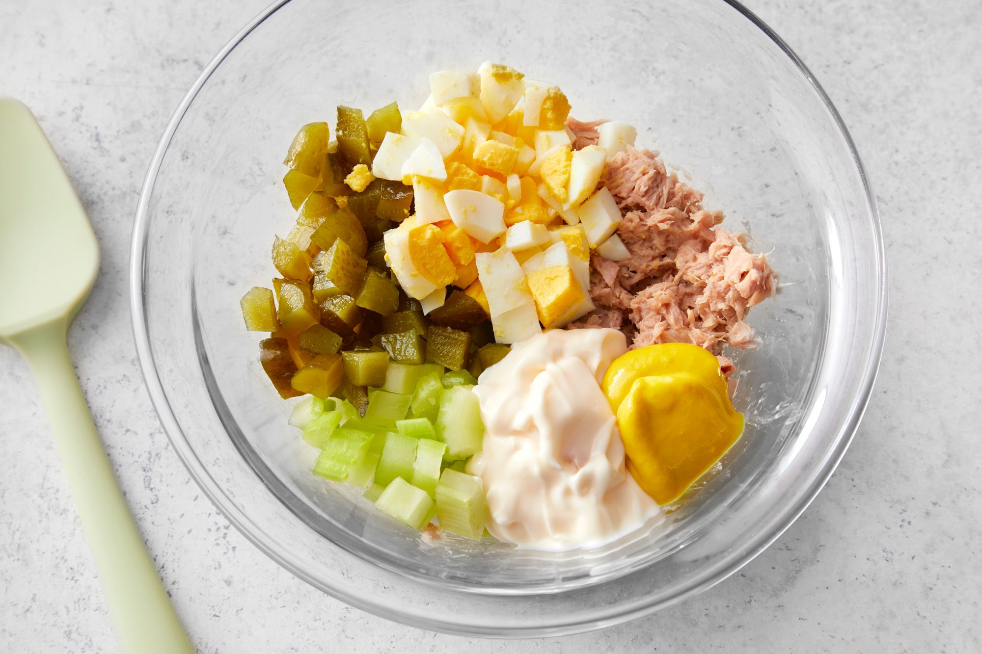 Overhead shot of all ingredients for Tuna Salad With Egg in a large mixing bowl; marble background;