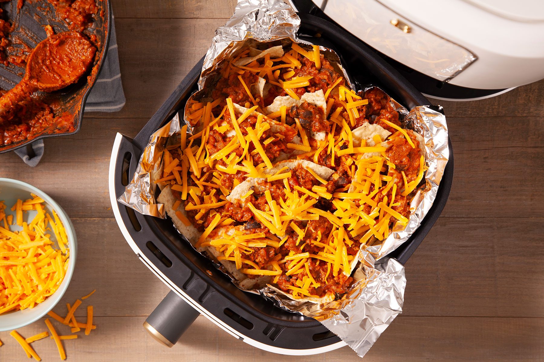 Nachos dressed and topped with cheese on foil layer in air fryer