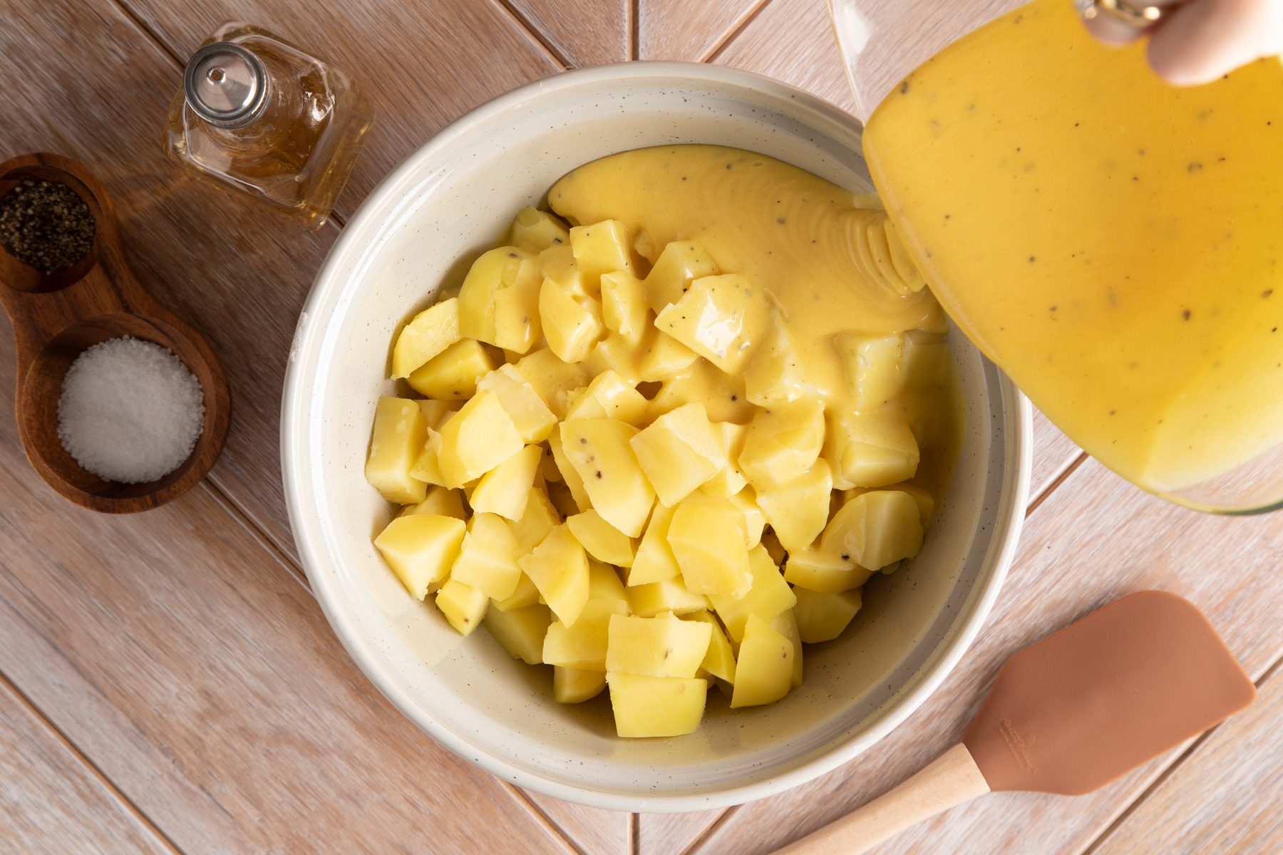 A person drizzling dressing over the potatoes