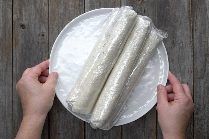 Overhead shot of roll-up tighly; and wrap each in platsic; wooden backhround;