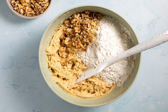 overhead shot; light blue textured background; added flour and walnuts in beaten mixture in a large bowl;