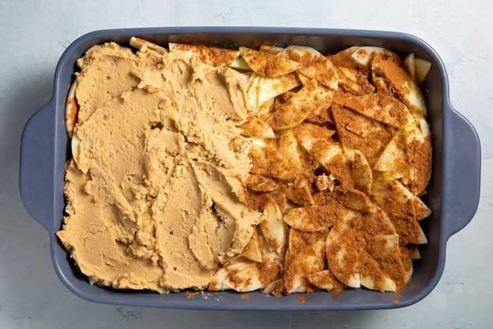 overhead shot; light blue textured background; spreaded beaten mixture over half part of apples in baking dish;