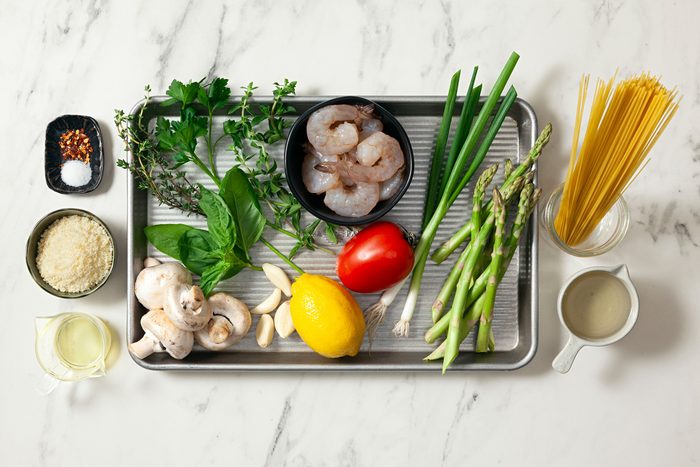 Shrimp, asparagus, angel hair pasta, tomatoes, and assorted ingredients arranged on a kitchen countertop