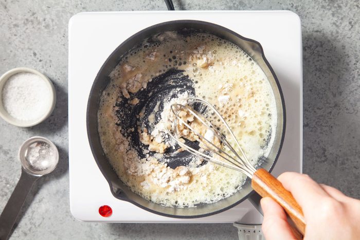 Overhead shot of whisk in flour; salt and pepper until smooth; spoon; induction; marble background;