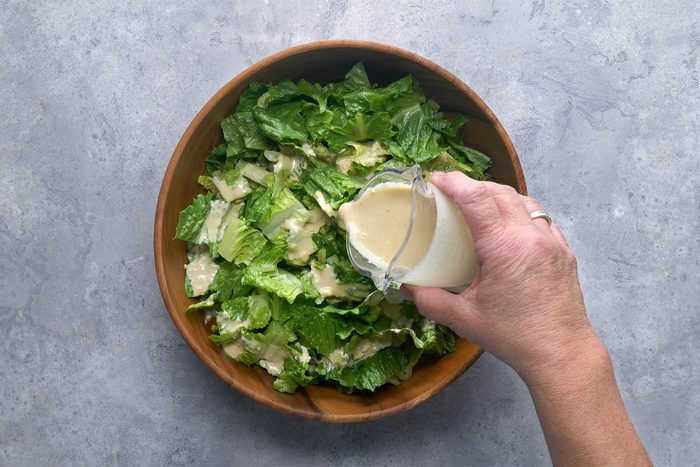 Overhead shot of place romiane into large salad bowl; drizzle with dressing; grey background