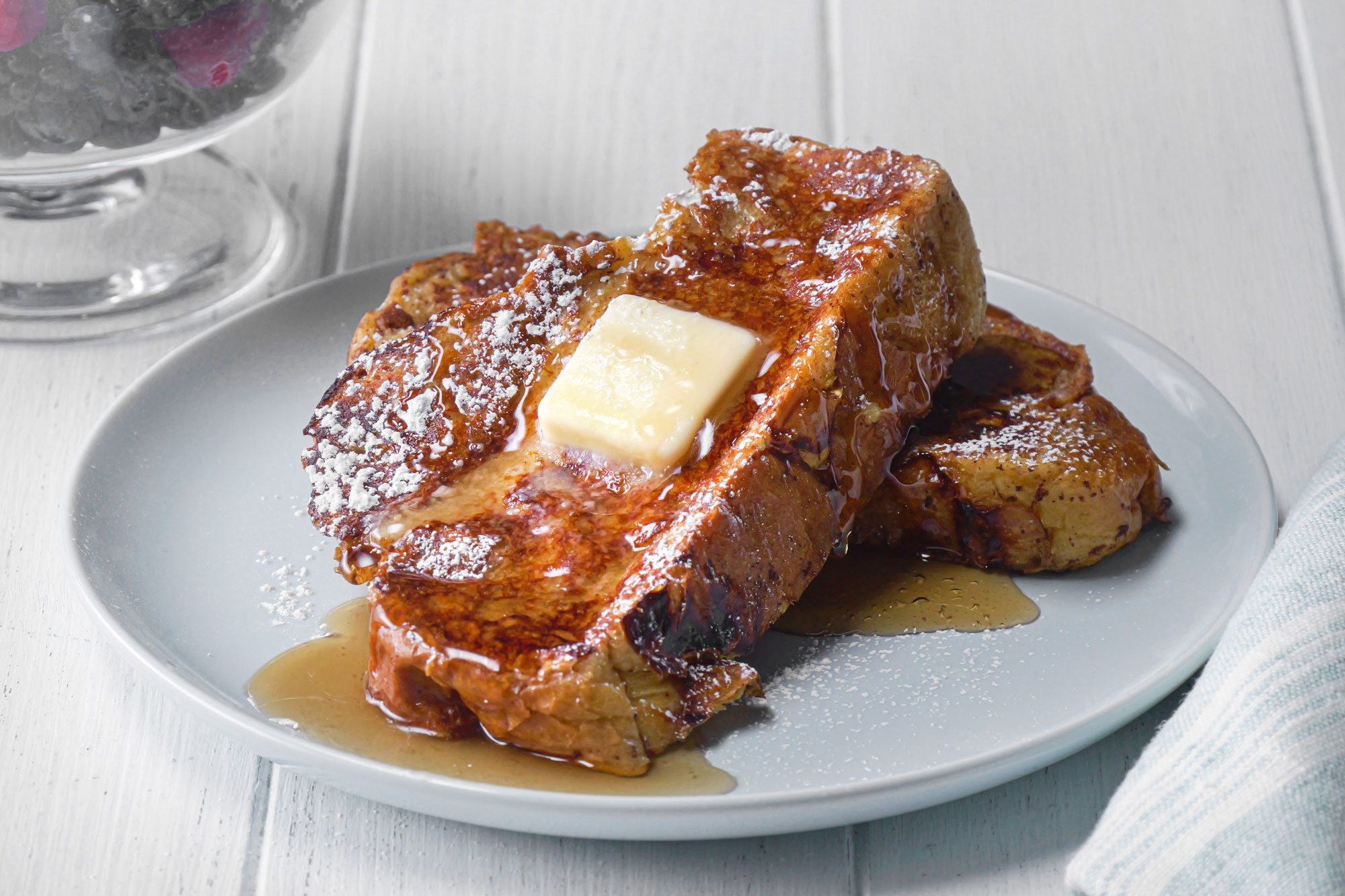 3/4th shot; white background; Challah French Toast; served on white plate; berries in bowl;