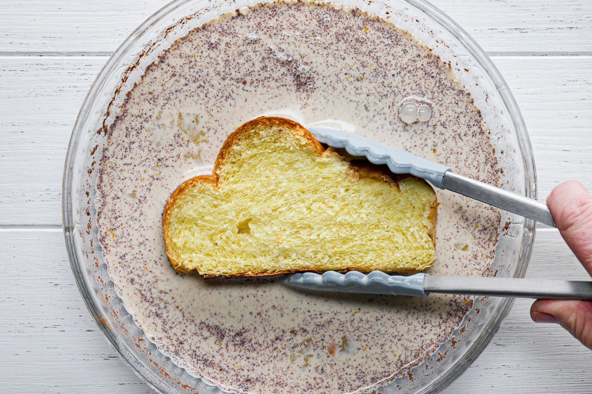 overhead shot; white background; dipping bread; into egg mixture; with tong;
