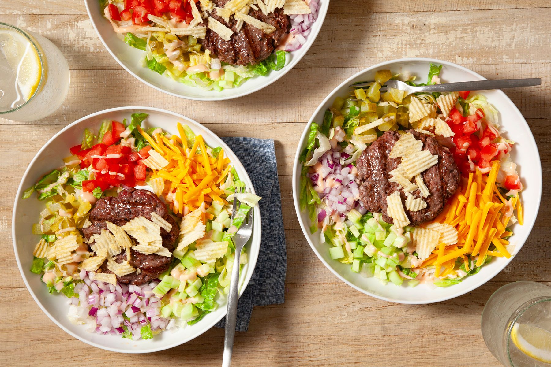 overhead horizontal shot; Cheeseburger Bowls placed over kitchen towel over wooden background;