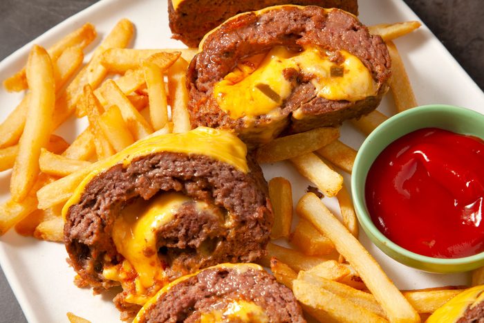Close shot of Cheeseburger Meat Loaf; cut into small round pieces; served on large platter with fries and ketchup; black texture background;