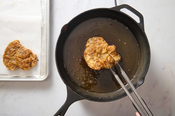 Image of chicken fried steak being fried in oil in a cast iron skillet
