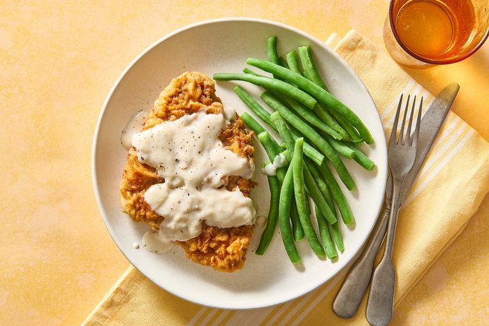 Overhead shot of chicken fried steak and gravy on a plate with some green beans