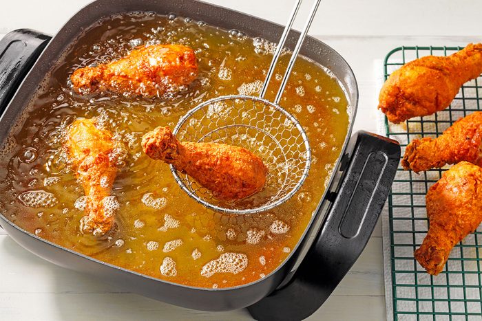 High angle view shot of electric skillet or deep-fryer; fry chicken; several pieces at a time; until chicken is golden brown and juices run clear; 7-8 minutes on each side; drain and placed on wire rack; wooden background;