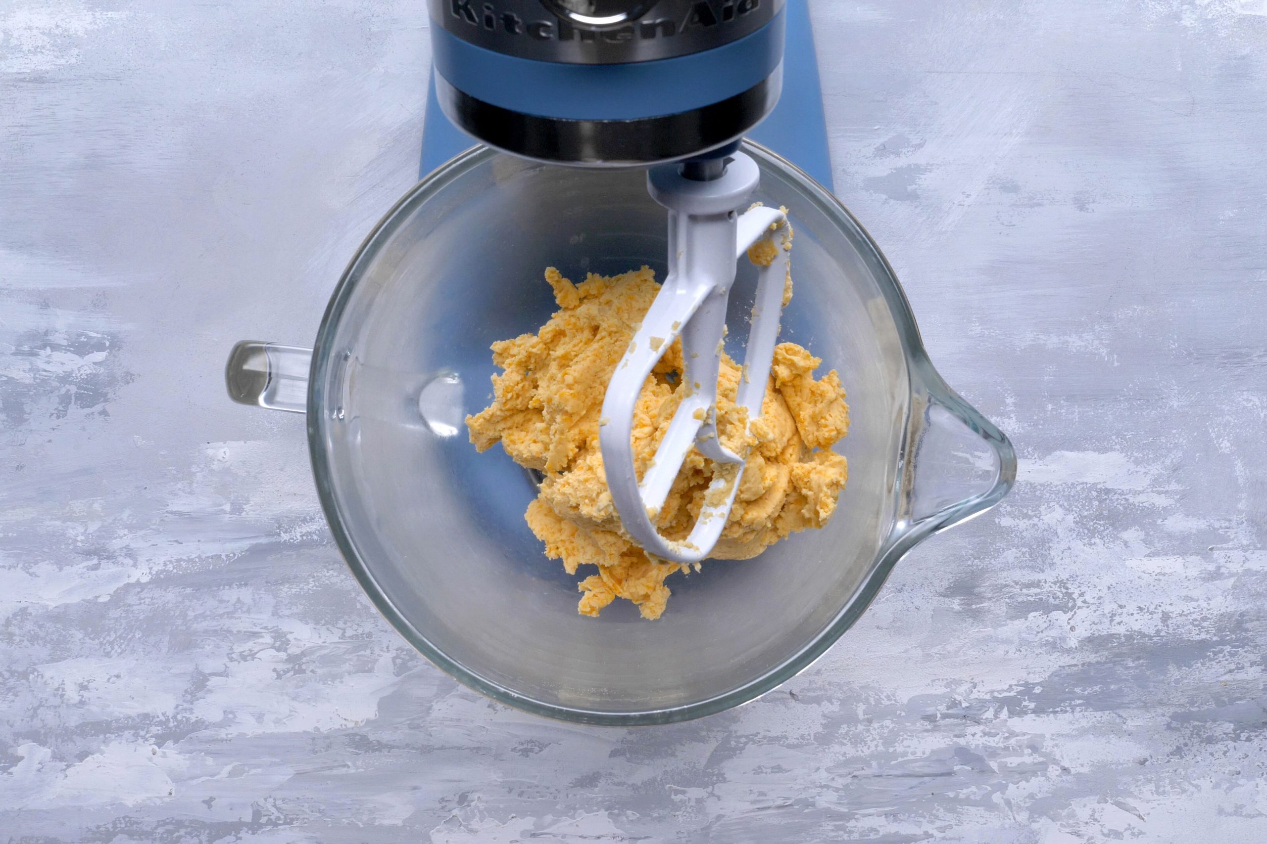 A hand mixer blending flour, salt, cayenne pepper and cheese in a mixing bowl.