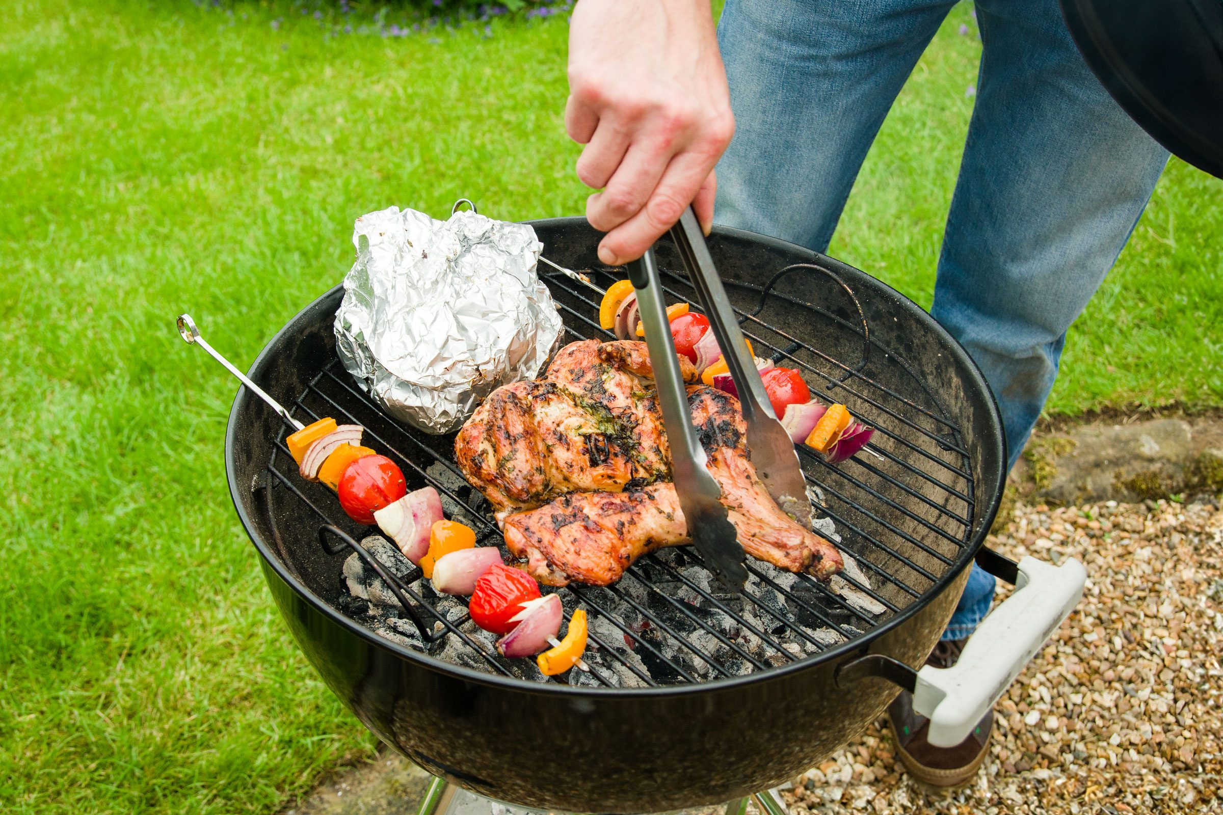 grilling meat and veggies on a charcoal grill in the grass during a summer picnic party