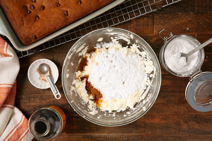 overhead shot of creamed cheese-butter, sugar, maple syrup, cinnamon and salt in a large glass bowl on wooden surface