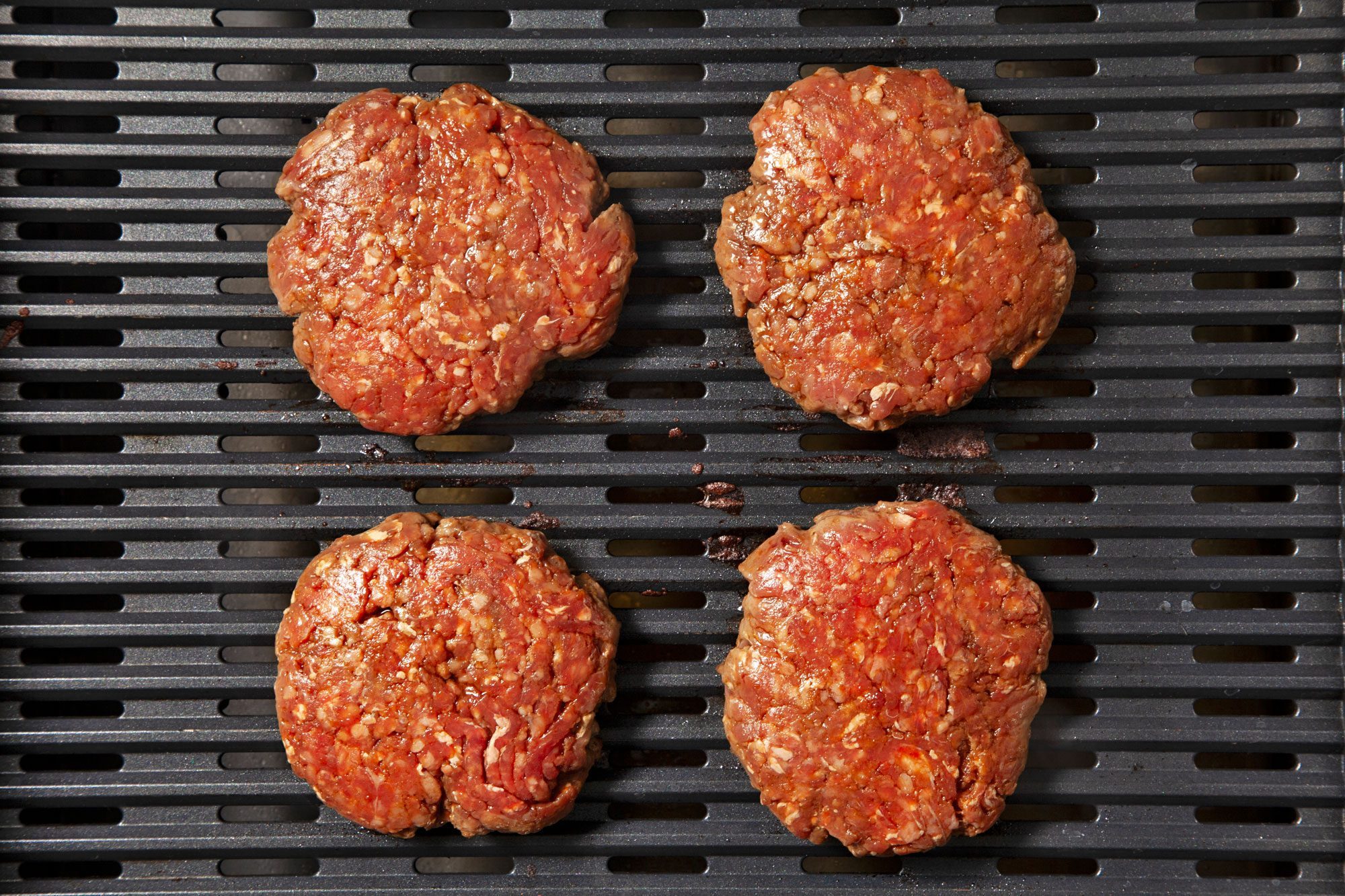 overhead shot; black background; grilling burger patties on griller;