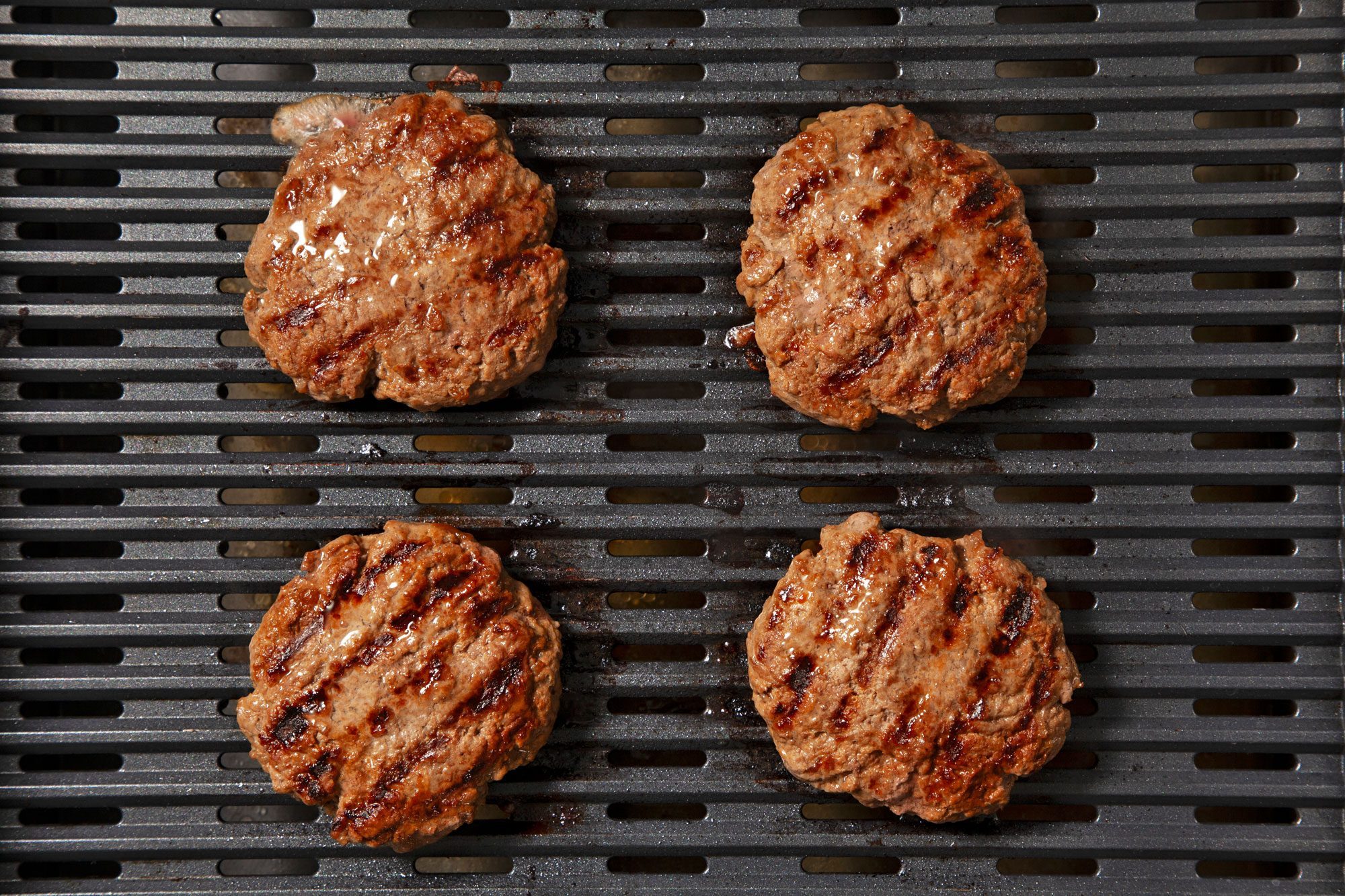 overhead shot; black background; grilling burger patties on griller;