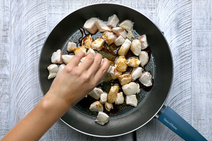 Overhead shot of a large nonstick skillet; heat two teaspoons oil over medium-high heat; stir-fry chicken and garlic 1 minture; add honey; soy sauce; salt and pepper; cook and stir until chicken is no longer pink; wooden background;