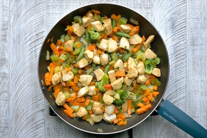 Overhead shot of a same skillet; return chicken to pan; stir cornstarch mixture and add to pan; bring to a boil; cook and stir until thickened; wooden background;