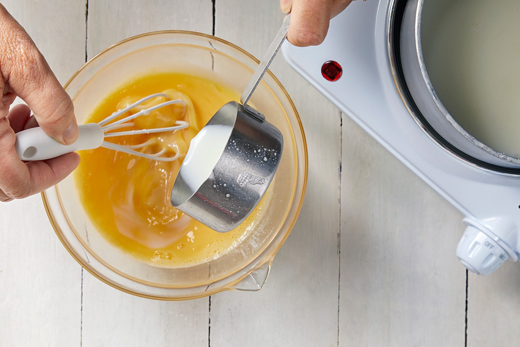 overhead shot; white background; in a small bowl, Whisking in a small amount of the hot mixture to the eggs;