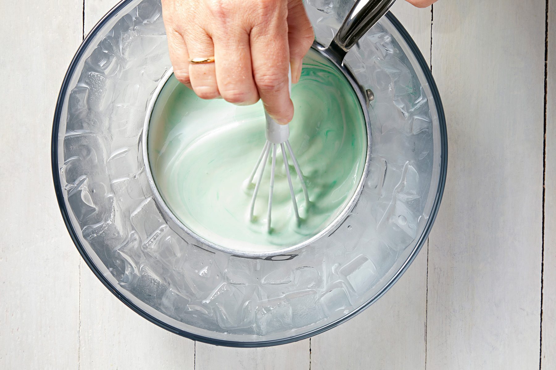 overhead shot; white background; cooling whipped cream in small saucepan placed in a bowl of ice and stiring the mixture;