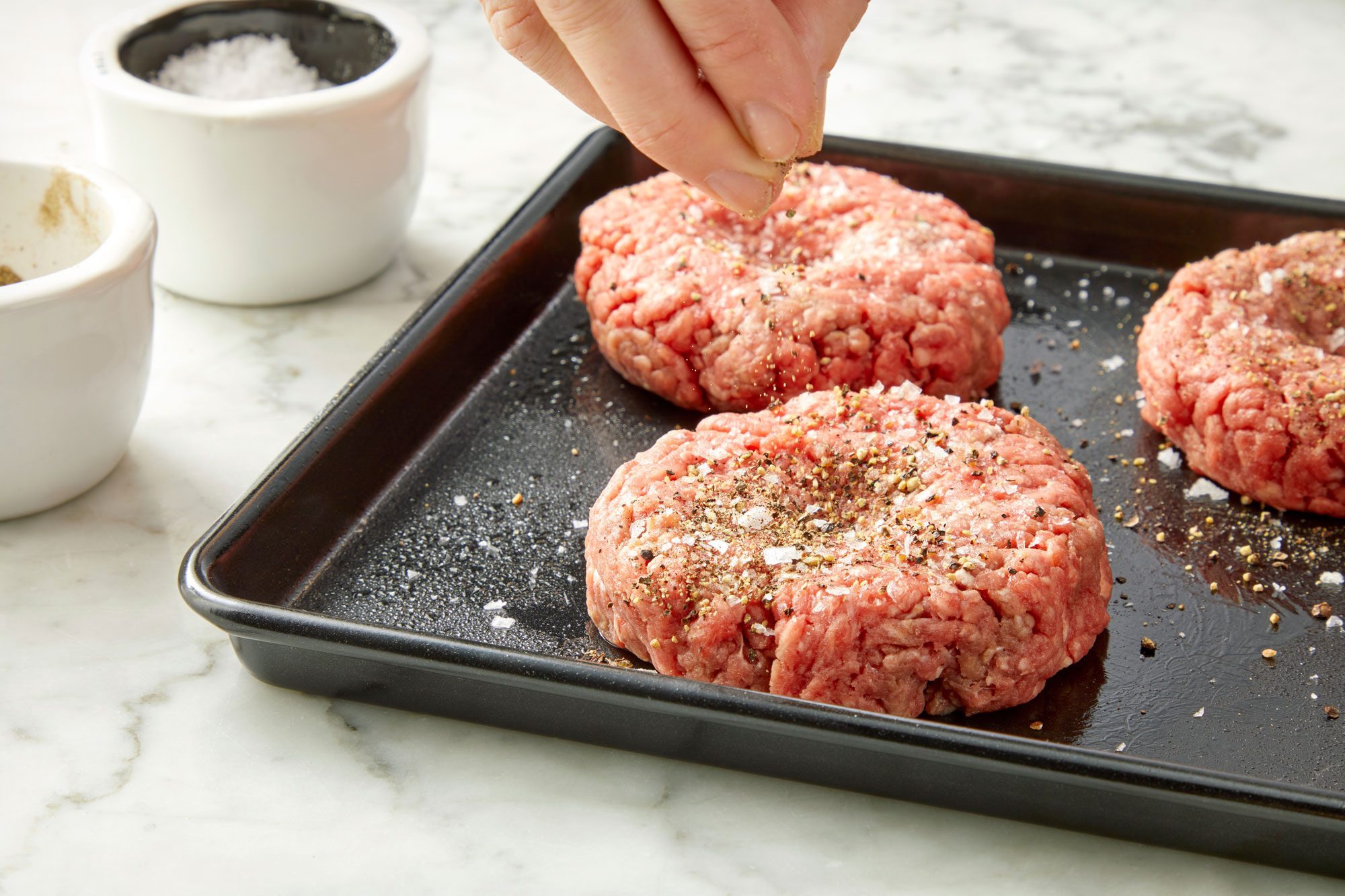 3/4 angle view shot of sprinkle both sides of patties with salt and pepper; baking sheet; marble background;