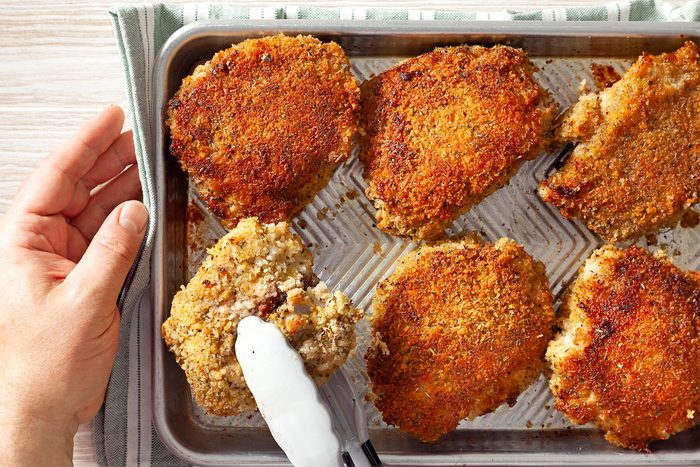 flipping baked chicken with tong in baking tray