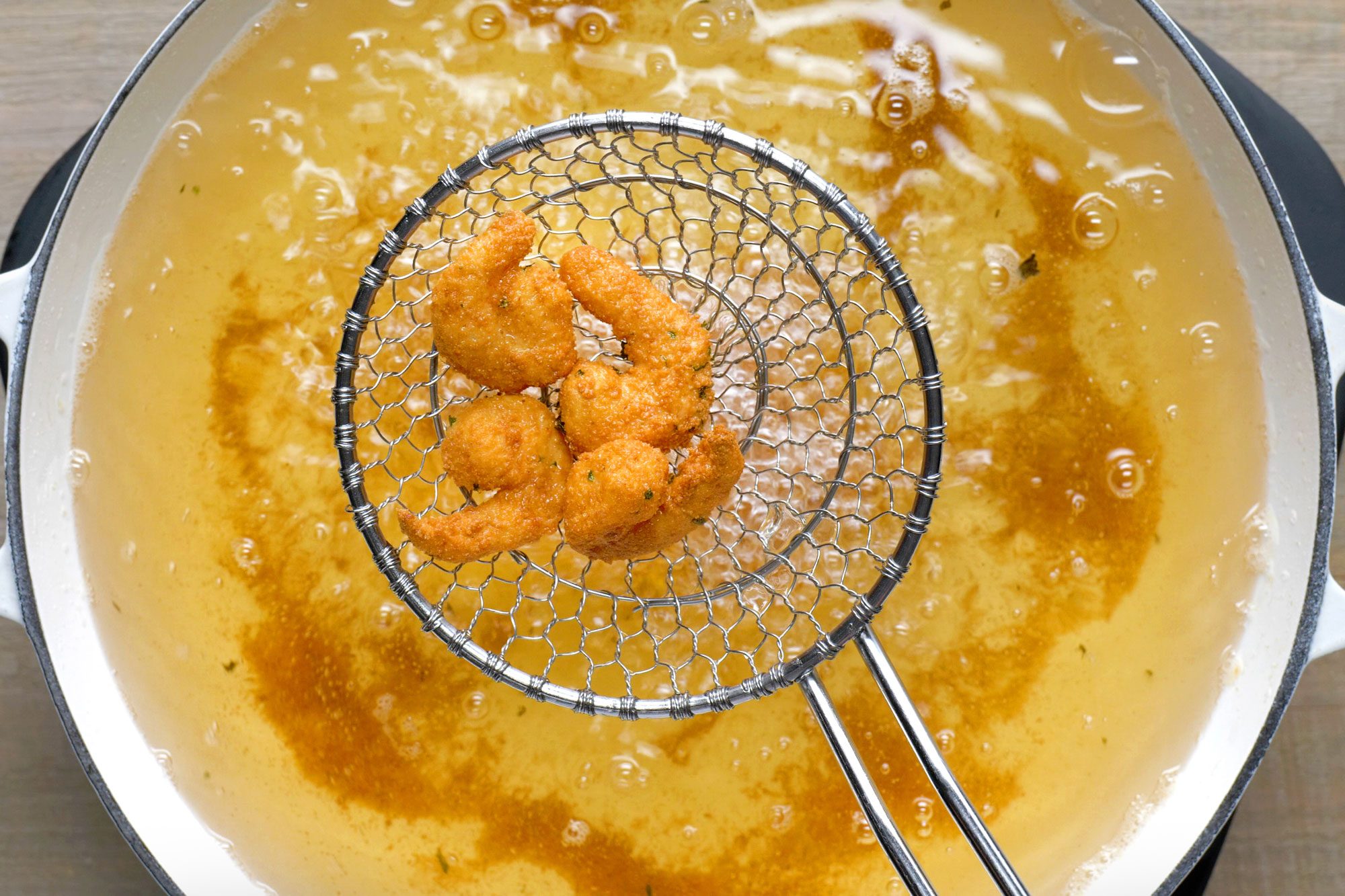Overhead shot of fry shrimp in batches until golden brown; large skillet; wooden background;
