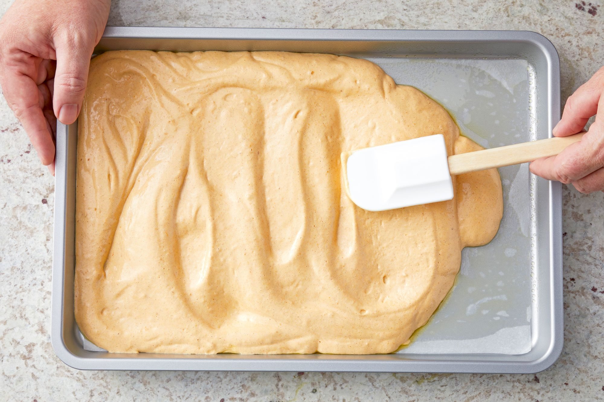 overhead shot; white textured background; spreading pumpkin mixture into baking dish with the help of spatula;