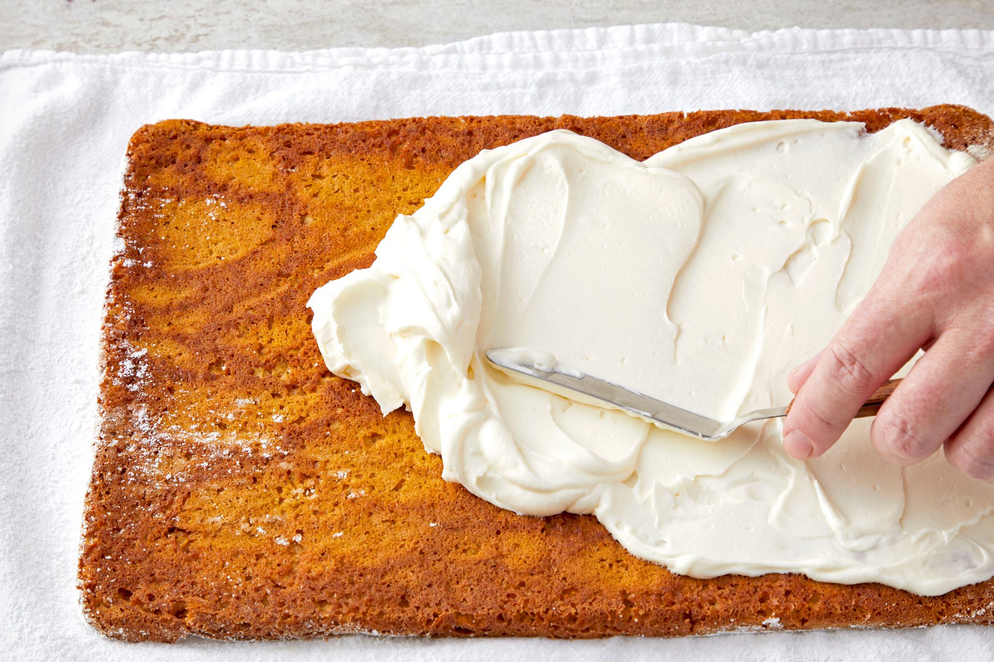 3/4th shot; spreading cream over cake with spreader;