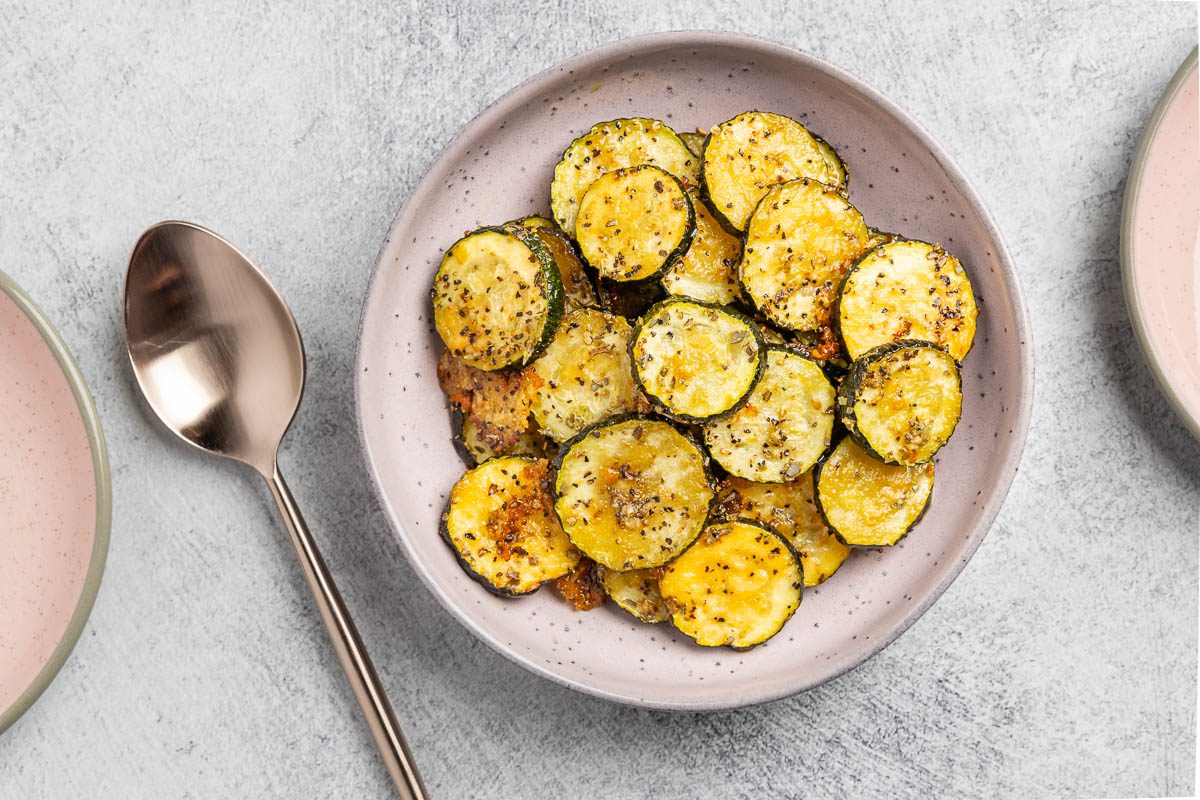 Taste of Home roasted zucchini recipe photo of roasted zucchini in a purple shallow bowl with rose gold spoon.