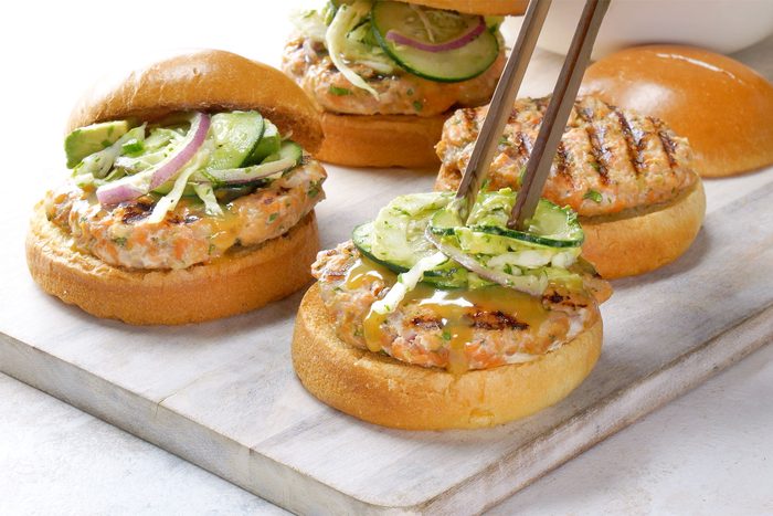 3/4 angle view shot of served on buns with honey mustard; top each with 1/2 cup slaw; wooden board; white marble background;