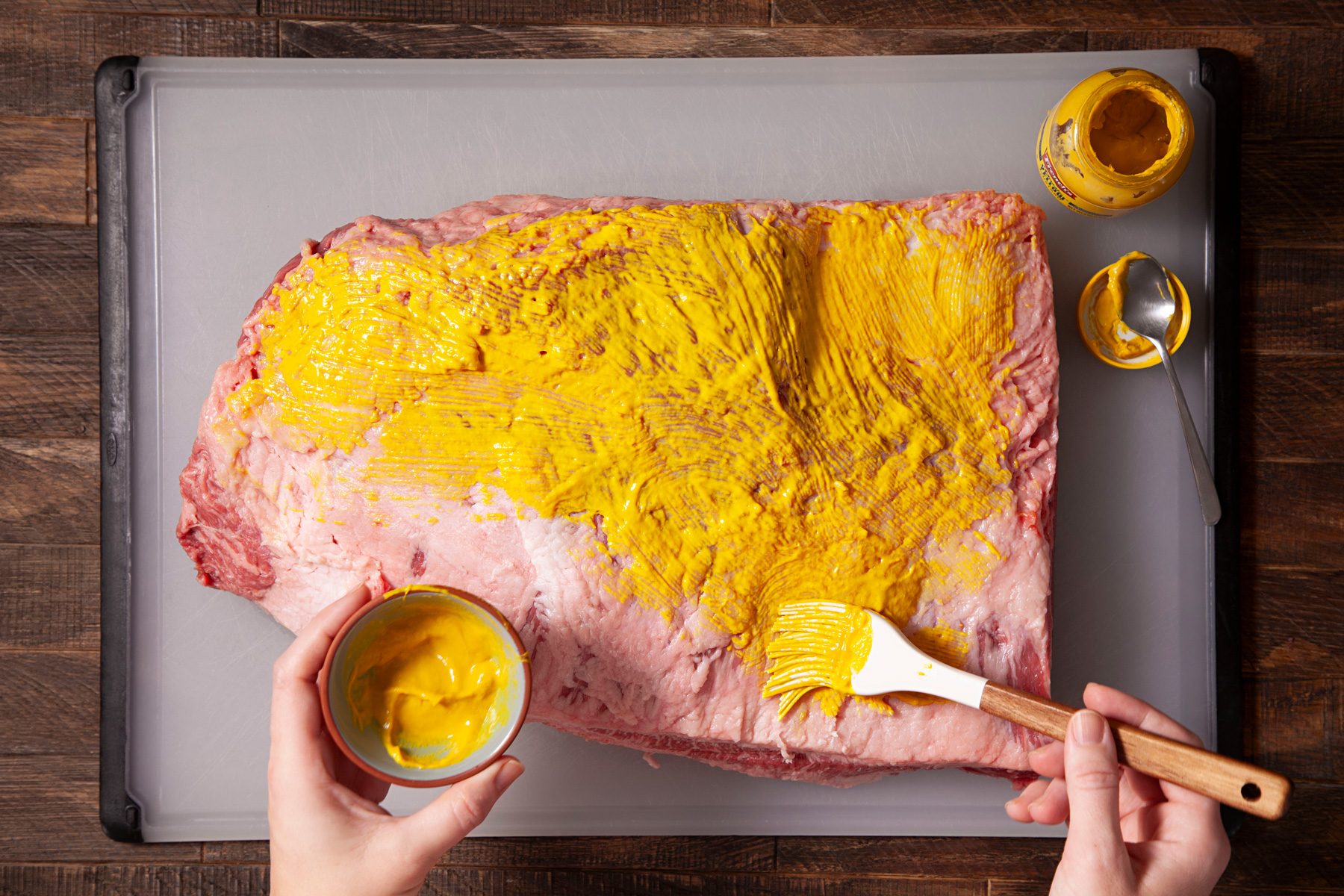 A person brushing the brisket with mustard paste