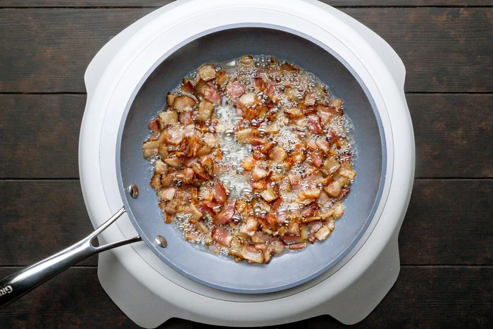 Chopped bacon is cooking in a large skillet