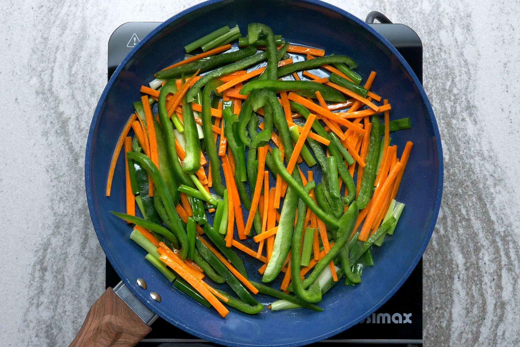 Sliced vegetables cooking in a blue wok
