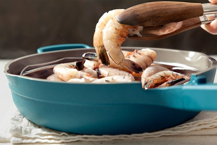 A person uses wooden tongs to pick up a shrimp from a blue pot filled with more shrimp